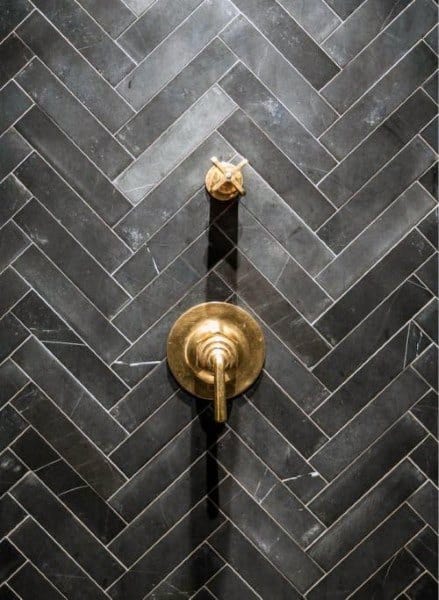 Black herringbone patterned tile shower with brass fixtures.