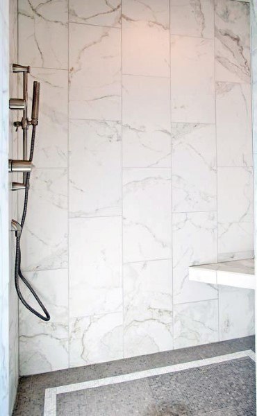 Shower with white marble wall tiles, mosaic floor tiles, and a handheld showerhead.