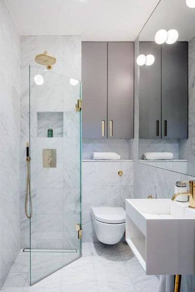 Modern bathroom with a corner glass shower, gray cabinets, white sink, and toilet; marble tiles adorn floor and walls