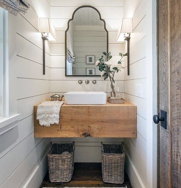 Rustic bathroom with wood vanity, arched mirror, and wicker baskets for storage.