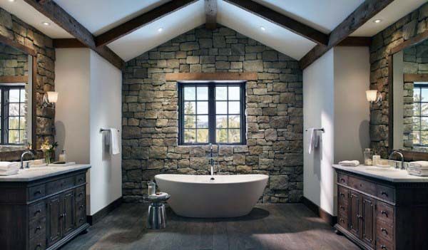 Rustic bathroom featuring stone wall, freestanding tub, wooden vanities, and beamed ceiling