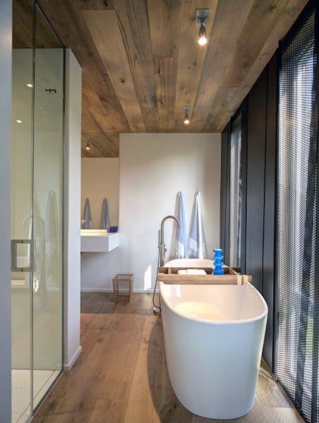 Modern bathroom with wood plank ceiling, freestanding tub, glass shower, and floor-to-ceiling windows.