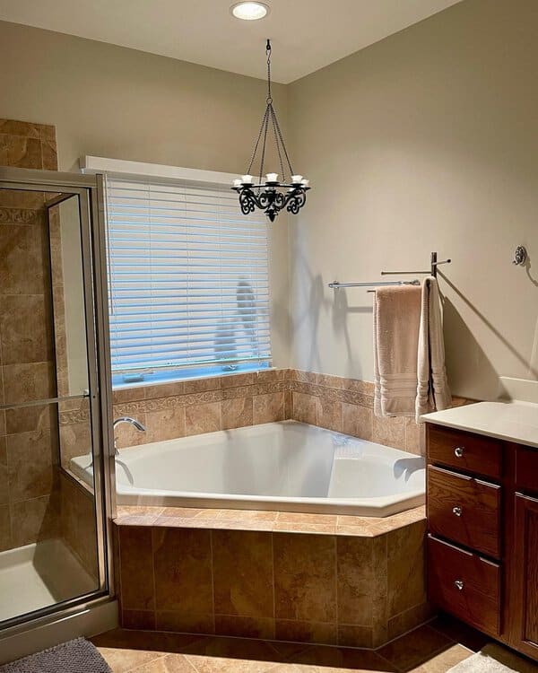 Wrought-iron chandelier above a corner tub surrounded by warm tile in a cozy bathroom.