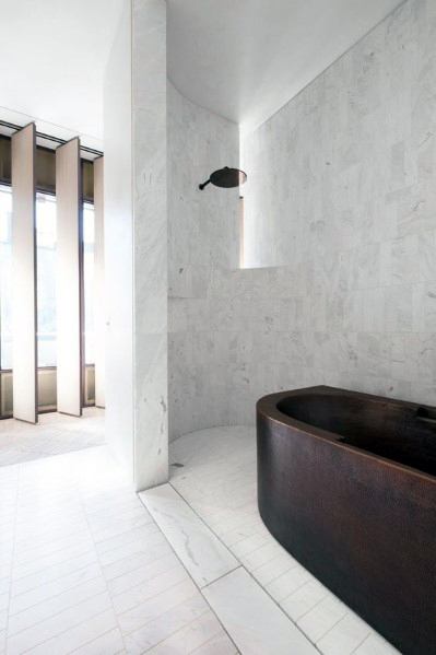Minimalist bathroom with white marble tile walls and dark freestanding bathtub.