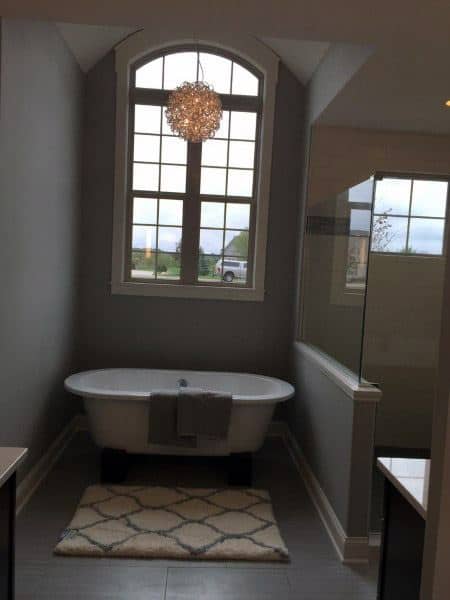 Elegant bathroom with free-standing tub, large window, and modern chandelier