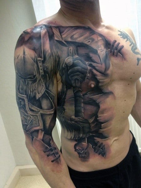 Man with a detailed warrior-themed tattoo covering his arm, shoulder, and chest