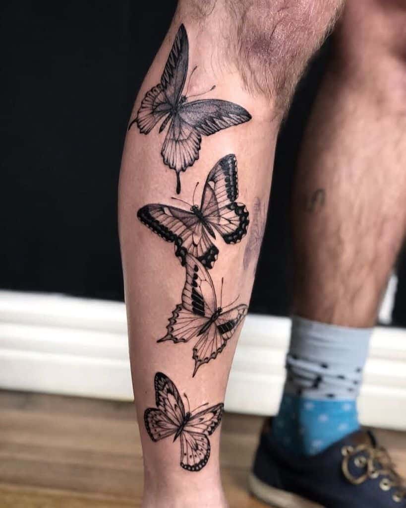 Black and gray butterfly tattoo on the lower leg, featuring four butterflies in flight with intricate shading and fine details.