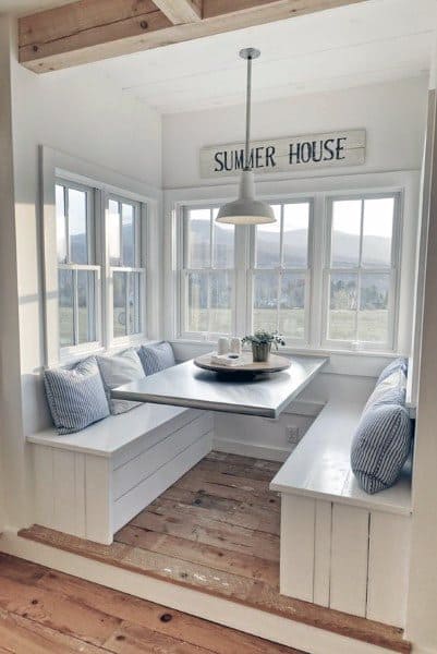 Cozy nook with a table, blue striped cushions, and a "Summer House" sign. Windows offer an idyllic view