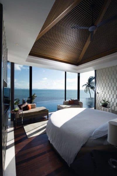 Tropical bedroom with wood ceiling, glass walls, and breathtaking ocean and palm tree views.