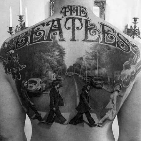 Black and gray full-back tattoo of The Beatles' Abbey Road scene, topped with a bold "The Beatles" logo and surreal illustrative elements.