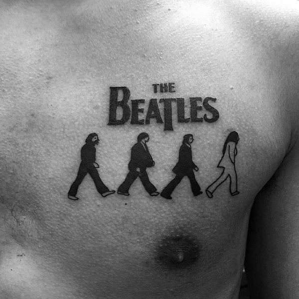 Chest tattoo of The Beatles' Abbey Road silhouettes beneath the band's iconic logo, with the final figure outlined instead of filled.