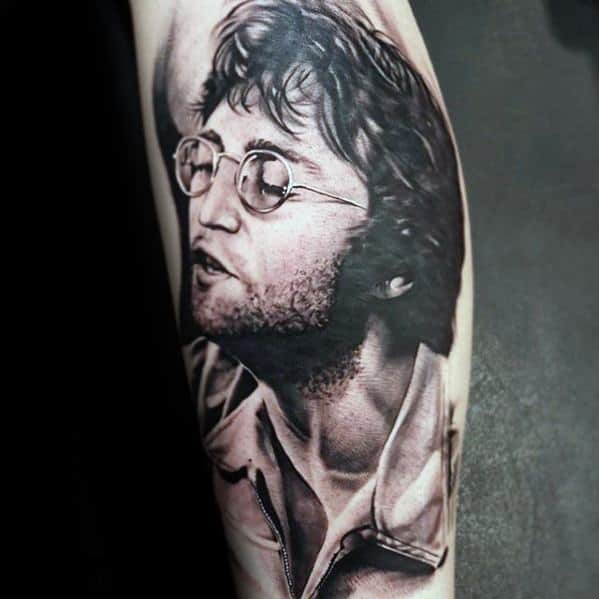 Realistic black and gray tattoo of John Lennon in a candid pose, featuring his signature glasses, tousled hair, and expressive facial detail.