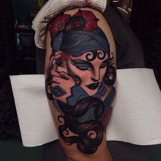 Bold tattoo of a gypsy woman with dark makeup, flowing hair, a headscarf, and intricate jewelry on the upper arm.