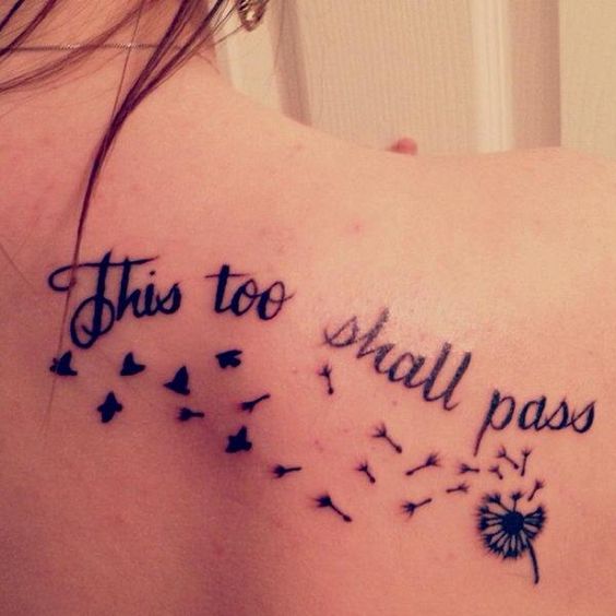 A "This Too Shall Pass" tattoo in cursive with flying birds and a dandelion design, on the upper back.