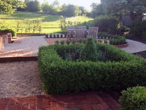 A formal garden with brick hedges, gravel paths, and a dining table with chairs