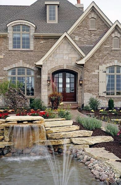 Elegant house exterior with brick and stone cladding, arched entry, and a serene garden pond with a cascading waterfall feature