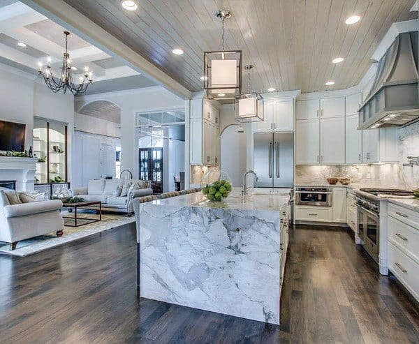 Modern kitchen with marble island, white cabinets, hardwood floors, and open living space.