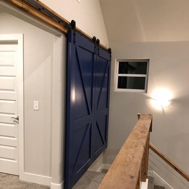 Blue double sliding barn doors with diagonal cross design on black hardware tracks.