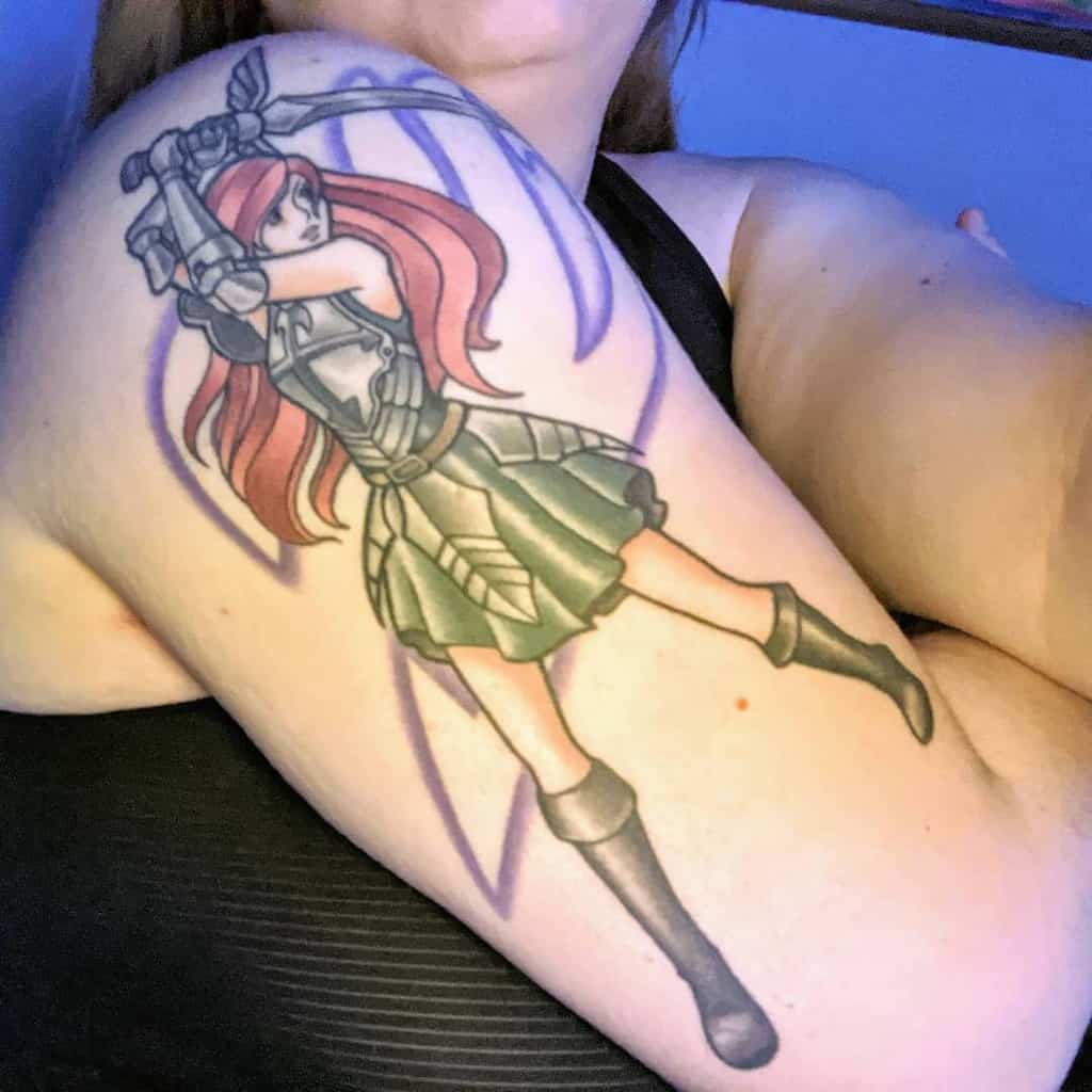 Colorful tattoo of Erza Scarlet from Fairy Tail on the upper arm, featuring her armored outfit, flowing red hair, and a bold sword-wielding pose.