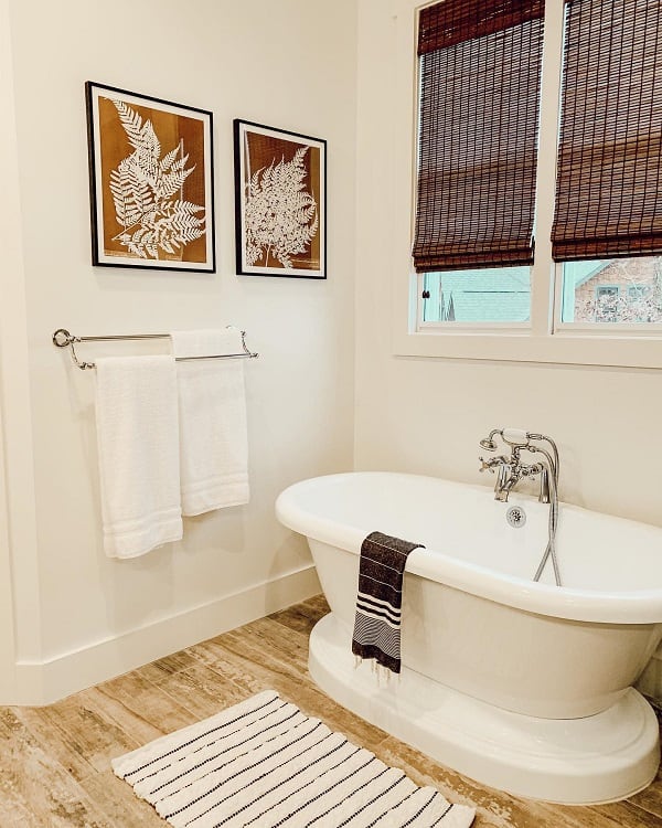 Minimalist bathroom with a white freestanding tub, fern artwork, and striped rug