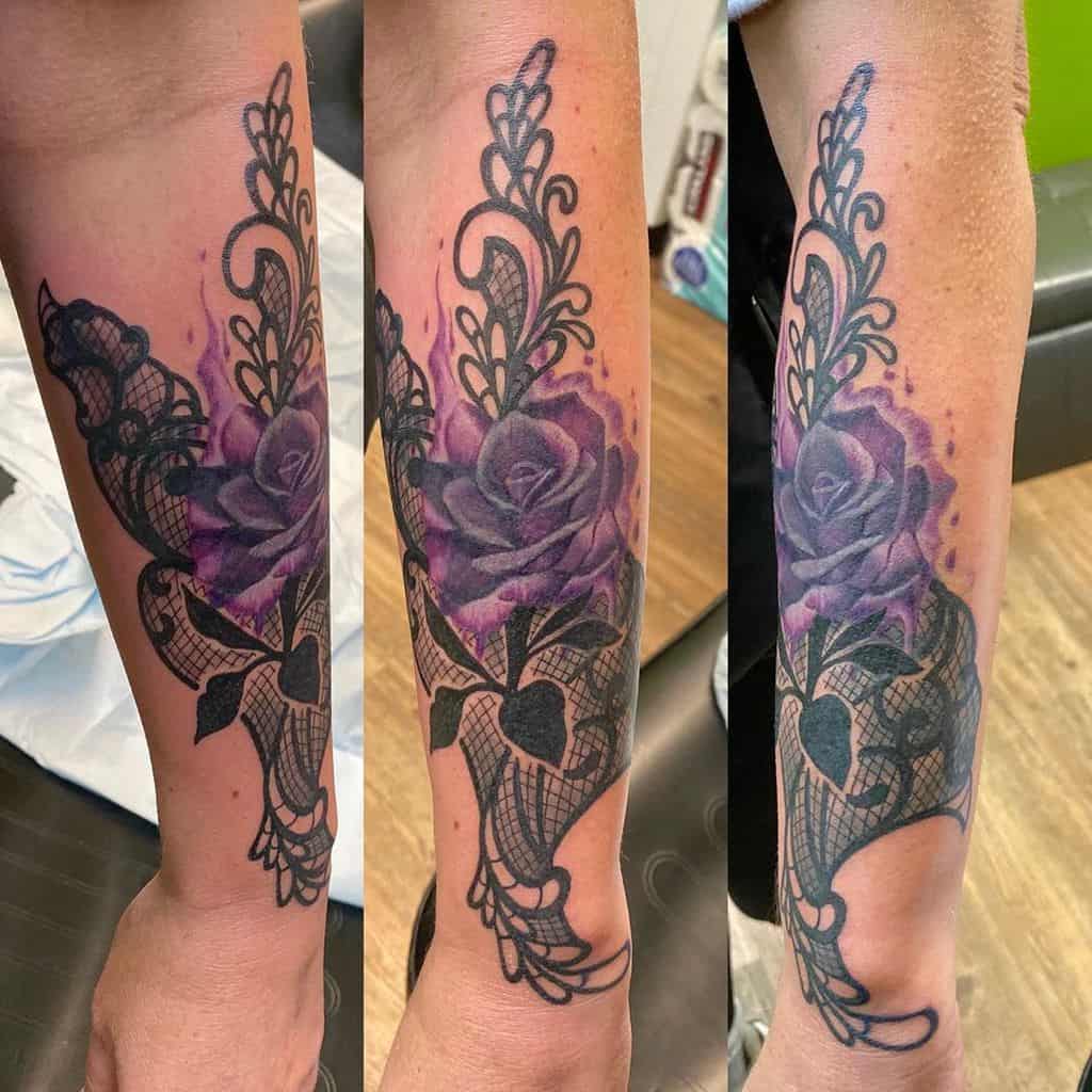 Elegant forearm tattoo featuring a vibrant purple rose with intricate black lace details, ornamental flourishes, and delicate shading.
