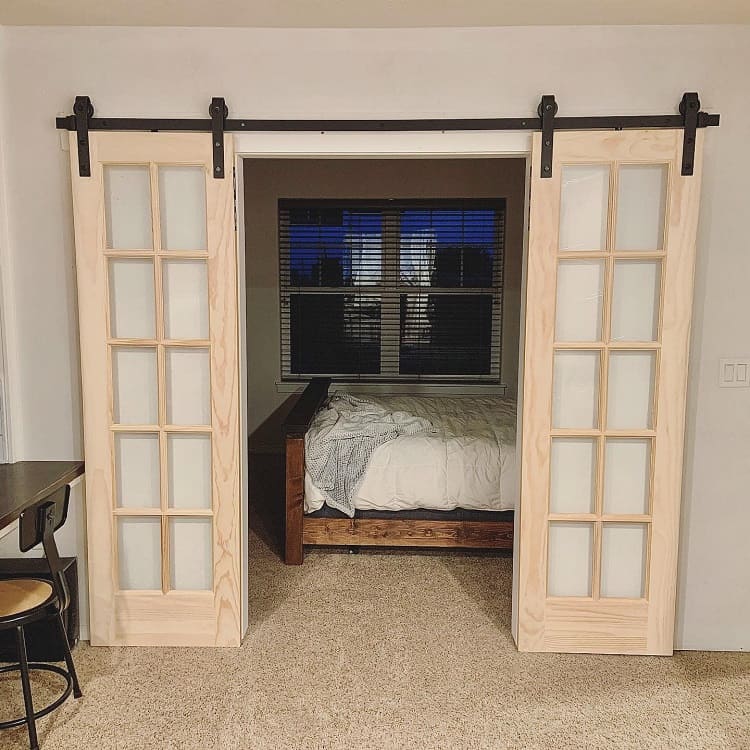 Wooden French-style sliding barn doors with frosted glass panes leading to a cozy bedroom.