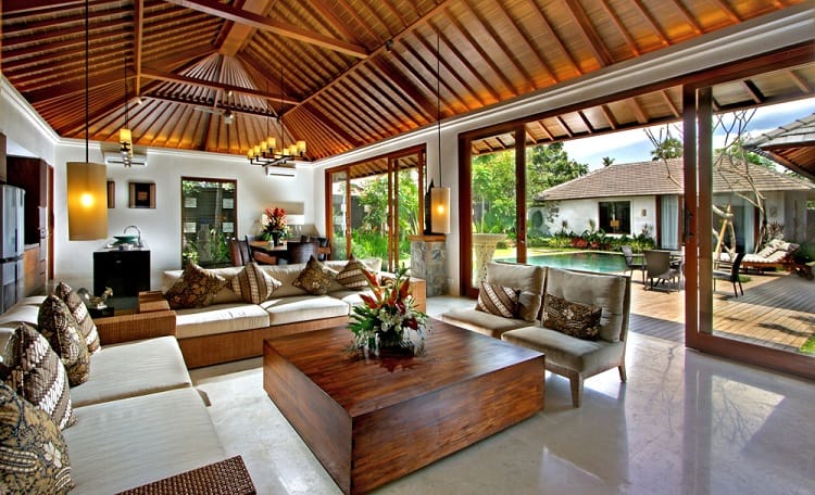A beautiful guesthouse living room with a vaulted ceiling, stylish furniture, and large glass doors that open to a tropical garden and pool area, creating a relaxing and open space