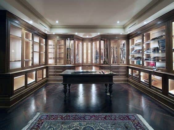 Luxurious gun room featuring elegant wood-framed illuminated display cabinets, a central table, and a decorative rug on polished hardwood flooring.
