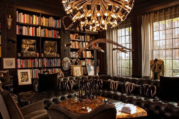 Luxurious library with dark furniture, bookshelves, a unique chandelier, and a dinosaur skeleton aloft