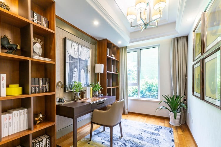 A stylish home office featuring wooden shelves, a desk, modern artwork, and a tray ceiling, creating a bright, productive space