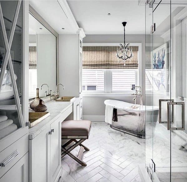 Elegant bathroom with a silver freestanding tub, chandelier, and marble flooring.