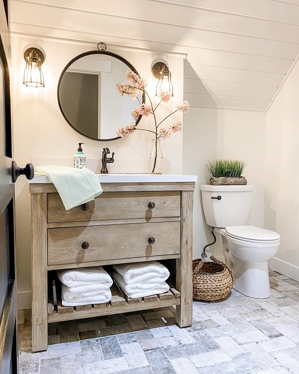 Cozy farmhouse bathroom with wooden vanity, round mirror, and potted plants; soft lighting creates a warm atmosphere