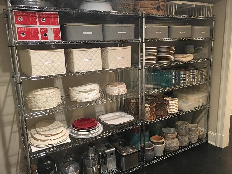 Metal shelves with baskets, plates, and kitchenware neatly arranged in a storage room.