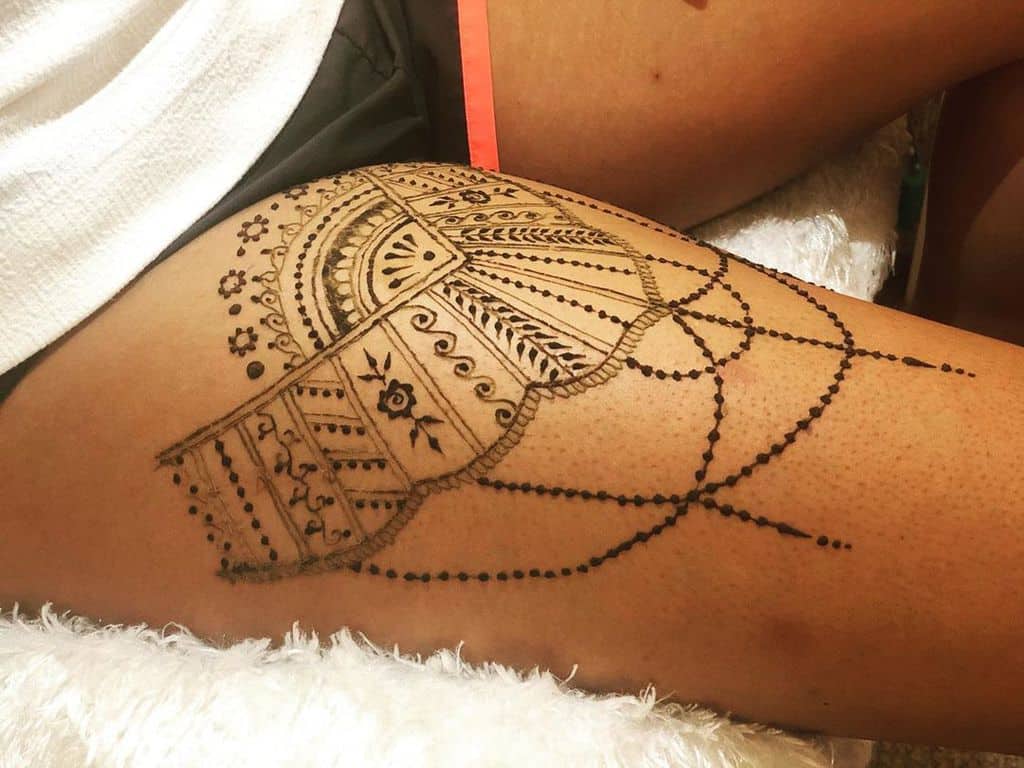 Ornate lace-inspired thigh tattoo with delicate patterns, floral motifs, and dotted chain details for an elegant and feminine look.