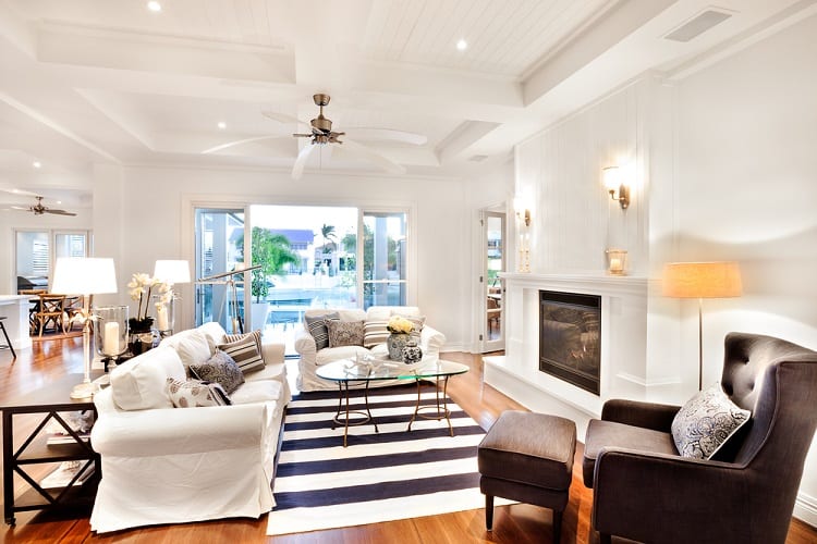 A beautiful living room with a coffered ceiling, elegant furniture, a cozy fireplace, and large windows that open up to a poolside view, creating a light and airy atmosphere