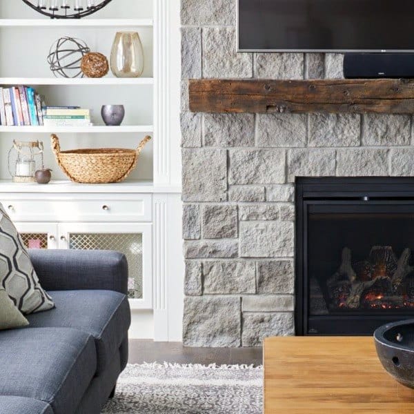 Cozy living room with stone fireplace, wooden mantel, and built-in white shelving.