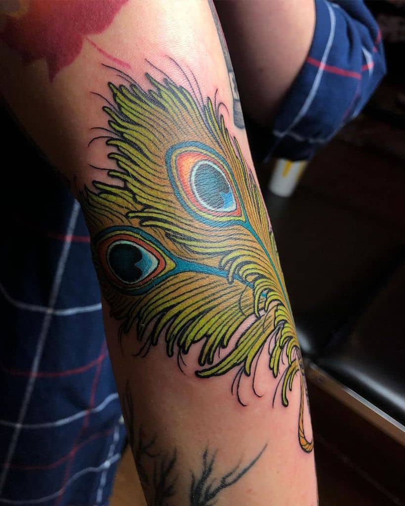 Bold and colorful peacock feather tattoo on the forearm, featuring vibrant greens, blues, and oranges with intricate detailing and shading.