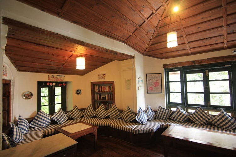 The ceiling features a charming wooden design with exposed beams, complementing the cozy, rustic atmosphere of the room with its inviting bench seating and beautiful view