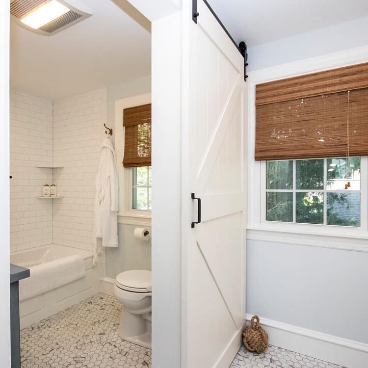 White sliding barn door with black hardware leading to a bathroom with subway tile and hexagon tile flooring.