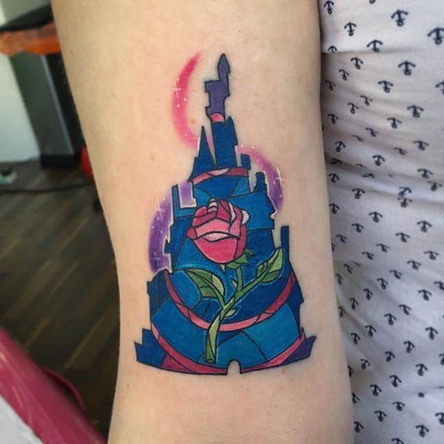 Stained glass-style tattoo of the Beast’s castle with the enchanted rose at its center, set against a glowing moonlit background.