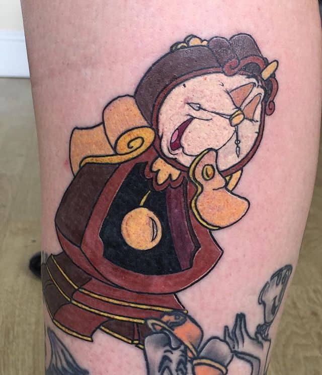 Tattoo of Cogsworth from Beauty and the Beast, showing his classic worried expression with bold outlines and vibrant colors.