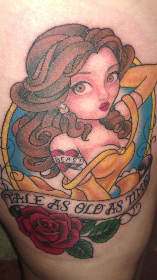 Tattoo of Belle in a vintage pin-up style, featuring a 'Beast' heart tattoo on her arm, a red rose, and a 'Tale as Old as Time' banner.