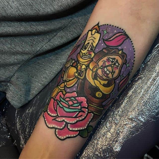 Colorful tattoo of Lumière and Cogsworth from Beauty and the Beast, with a bold pink enchanted rose and a vibrant stained-glass background.