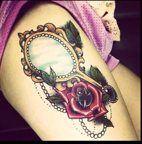 Elegant Beauty and the Beast-inspired tattoo featuring an ornate hand mirror, a red enchanted rose, green leaves, and pearl details.