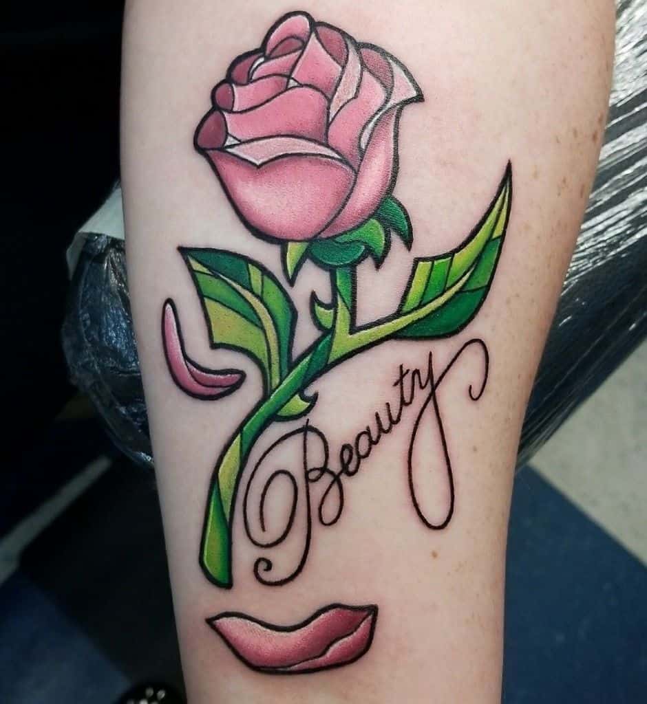 Tattoo of a pink enchanted rose with 'Beauty' written in elegant script, accented with falling petals and a pair of lips below.