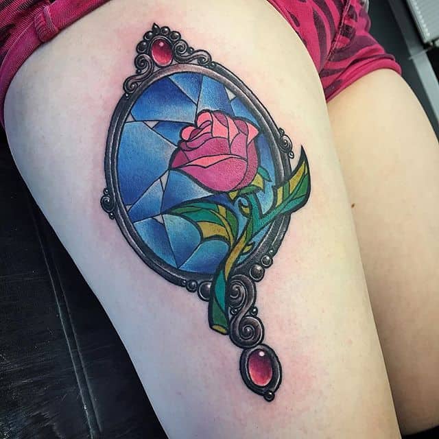 Stained glass-style tattoo of the enchanted rose within an ornate mirror frame, featuring rich colors and intricate detailing.