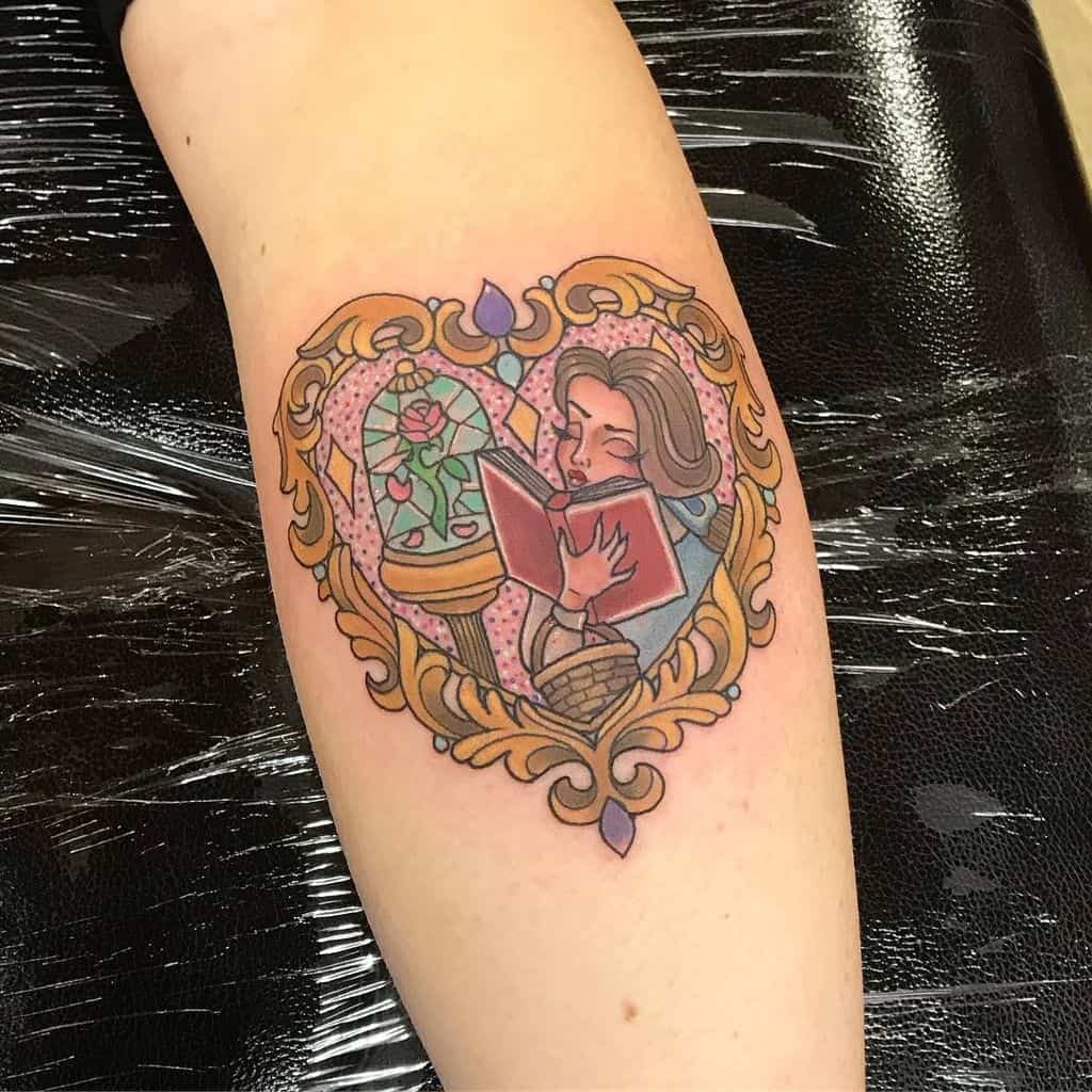 Heart-shaped tattoo of Belle reading a book, framed by an ornate golden border, with the enchanted rose in the background.