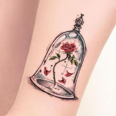 Delicate tattoo of the enchanted rose inside a glass dome, with fine-line details and soft red petals falling around it.