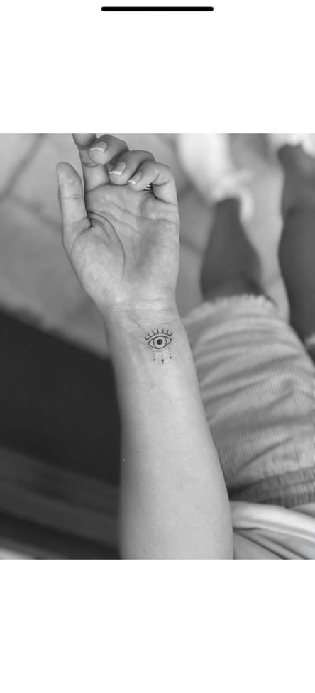 Small minimalist tattoo of an all-seeing eye with radiating lines, inked in black on the wrist.