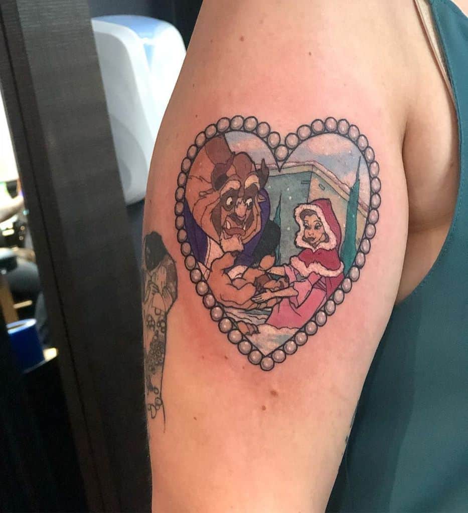 Heart-shaped Beauty and the Beast tattoo featuring Belle and the Beast in a snowy scene, framed with a pearl-like border.